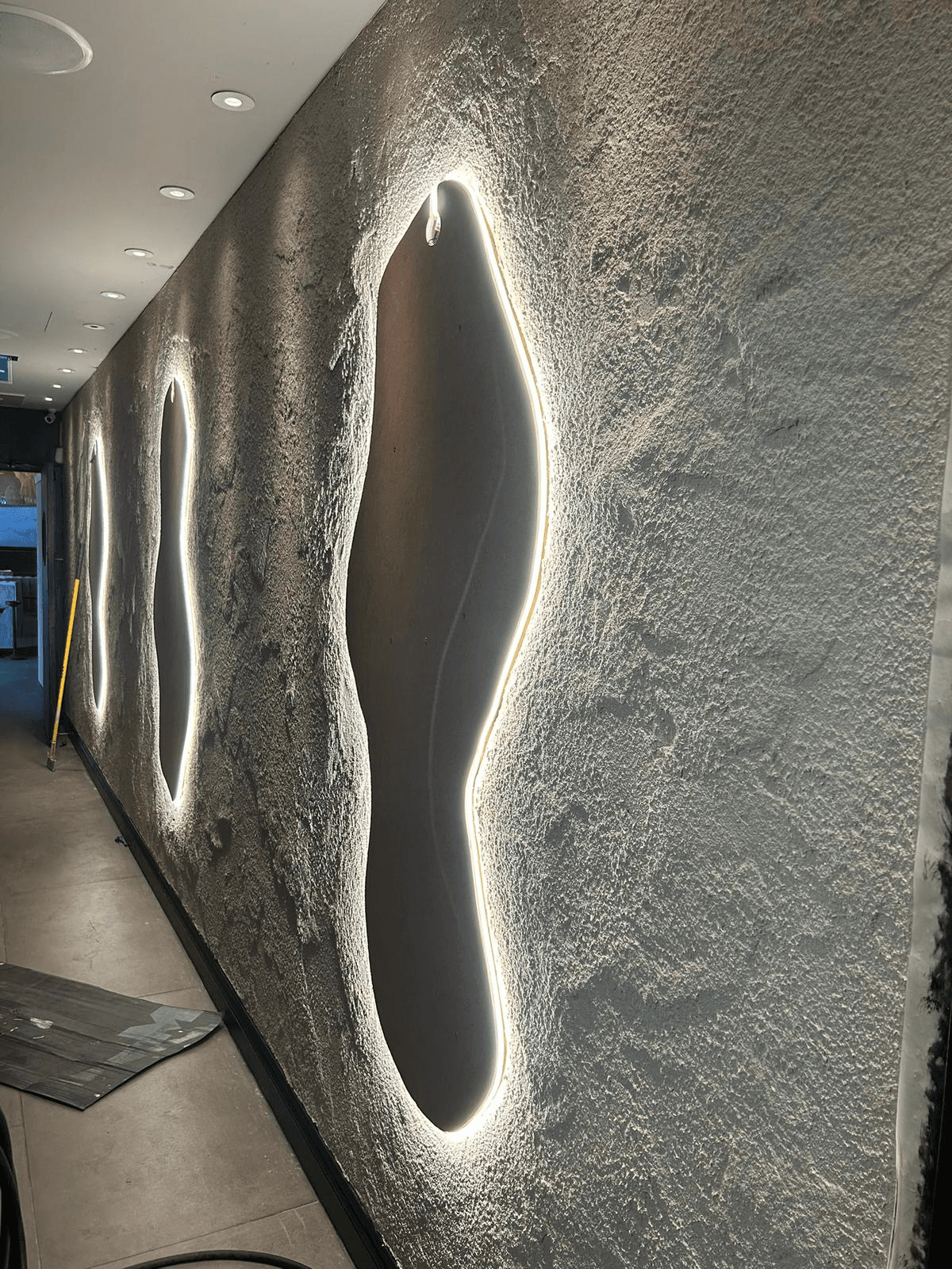 Decorative feature wall with backlit oval cutouts and recessed lighting in a commercial corridor