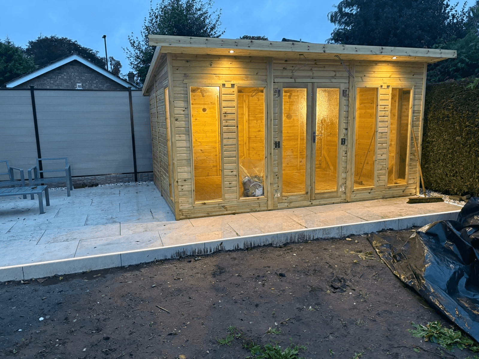 Garden room summer house with warm exterior lighting illuminating the facade at dusk