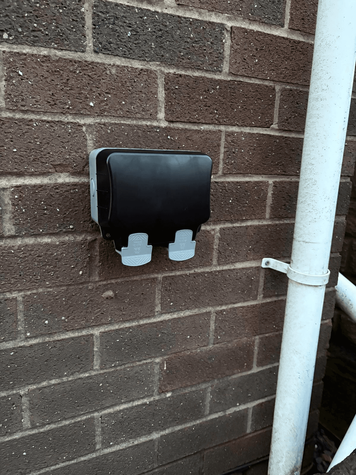 Outdoor weatherproof double socket mounted on exterior brick wall