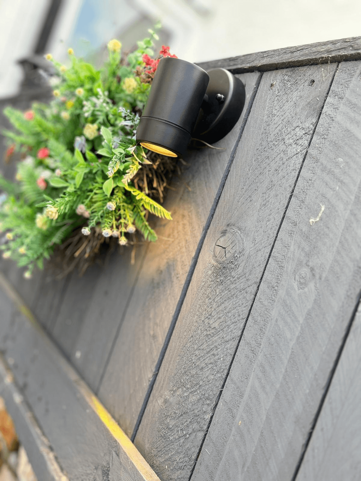 Black outdoor wall spotlight mounted beside a garden planter box on timber cladding