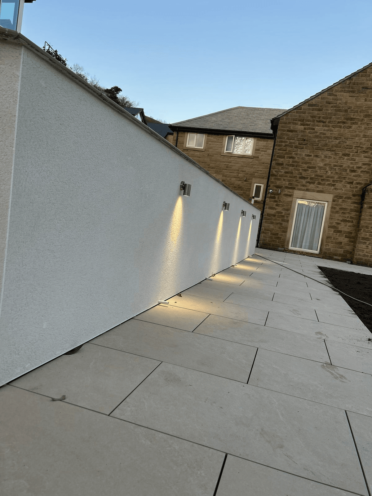 Row of outdoor wall downlights along rendered patio boundary wall at dusk