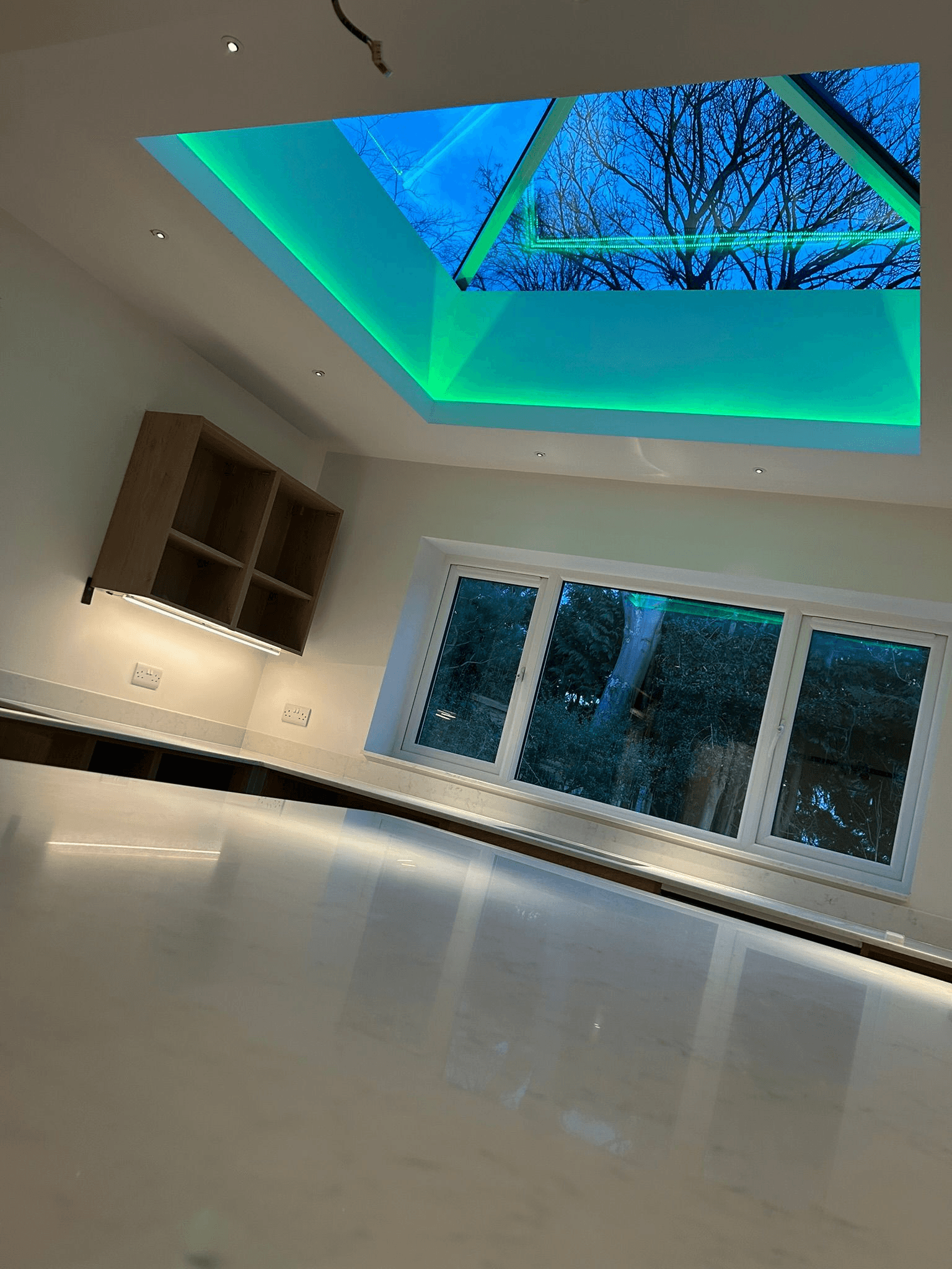 Indoor kitchen extension with green LED lighting around glass skylight roof lantern