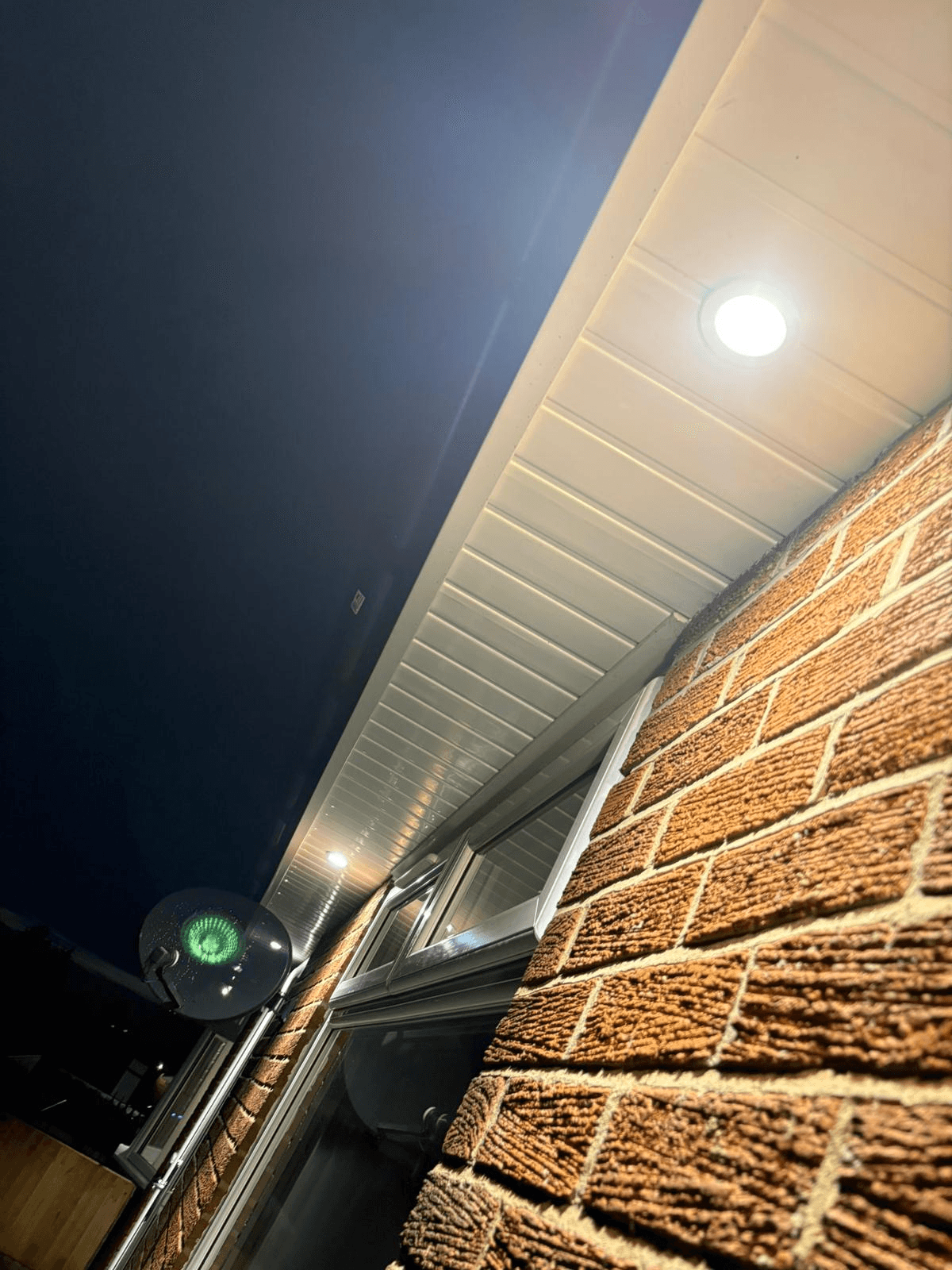 Recessed downlight fitted in soffit on brick building at night